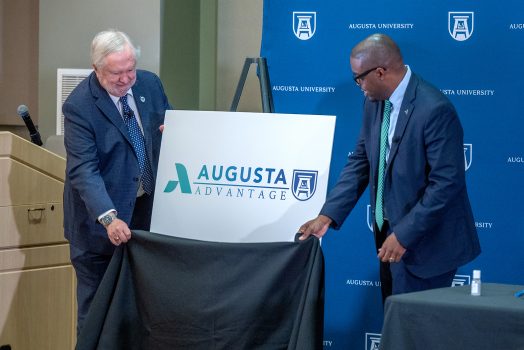 Two men unveil board with logo that says Augusta Advantage