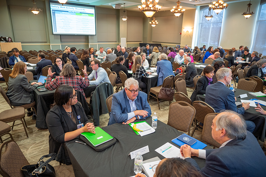 large group of people sit at tables in a large conference room