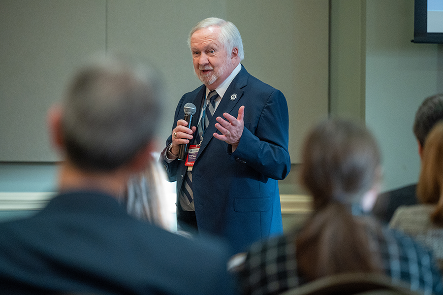 man in a suit holds a microphone while talking to a large group of people