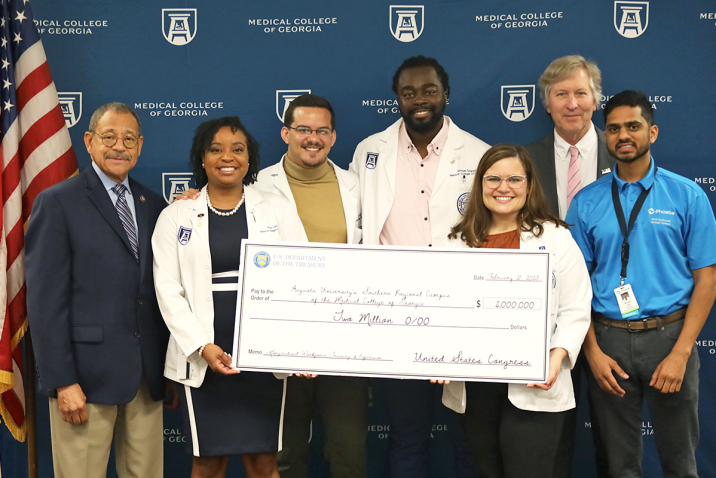 medical students in white coats hold a large commemorative check for a photo with three men