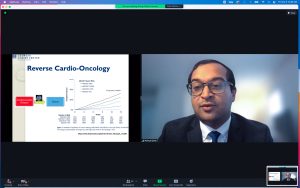 Split screen with powerpoint presentation on cardio oncology on left, man in black suit with glasses on right.