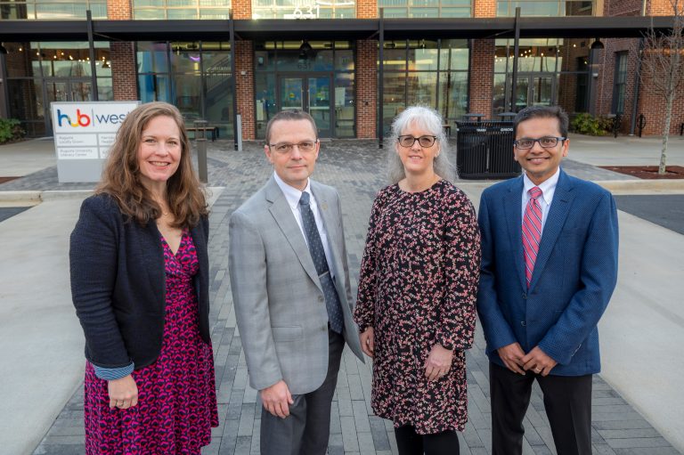 Four people stand in front of building smiling
