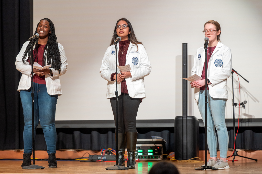 three female students in white coats singing