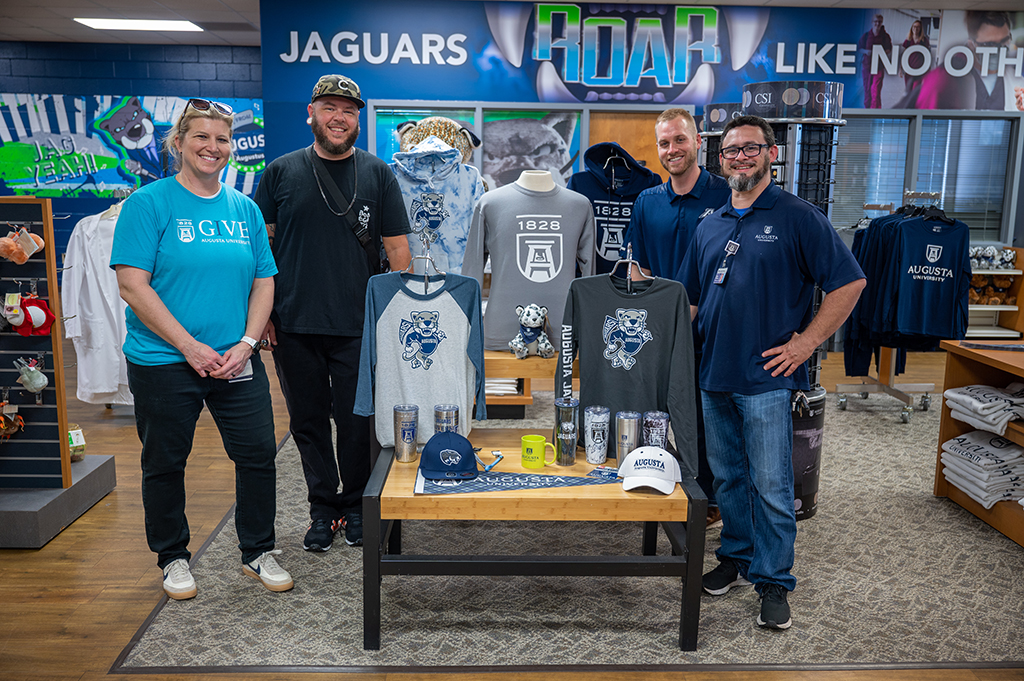 One woman and three men standing near AU merchandise