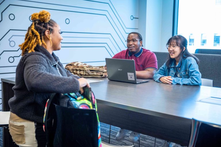 three people standing around a table with a computer