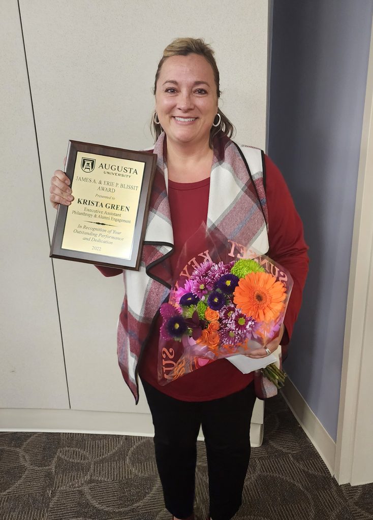 woman standing with flowers and an award
