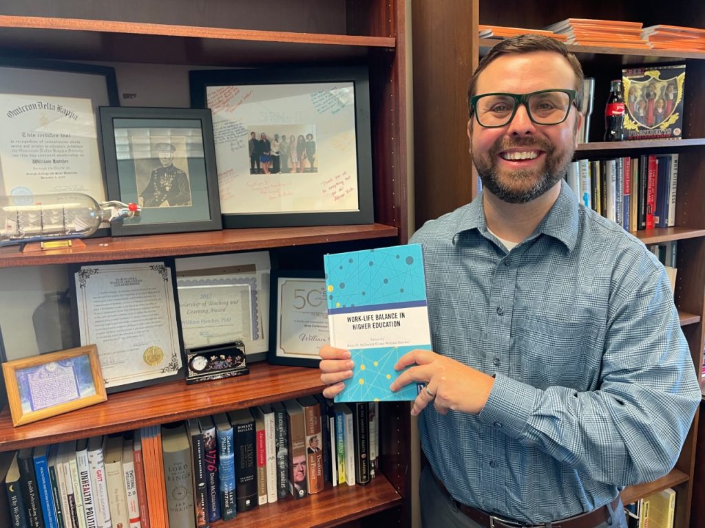 Man smiles while holding a book he wrote