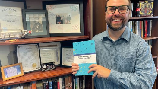 Man smiles while holding a book he wrote