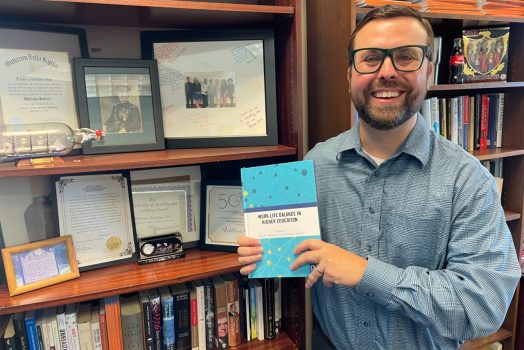 Man smiles while holding a book he wrote