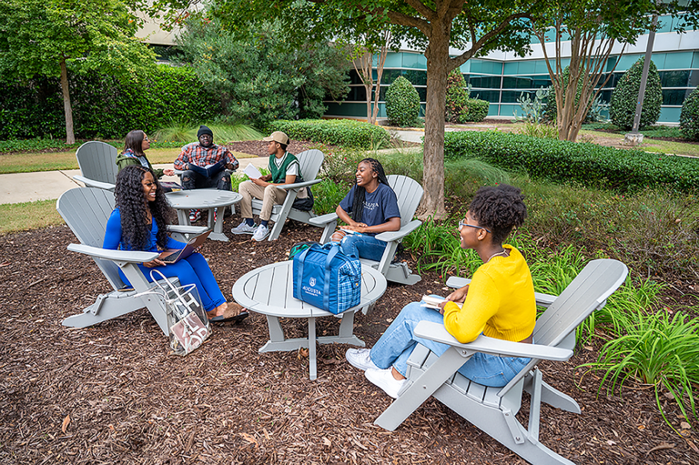 men and women outside talking while sitting in patio chairs