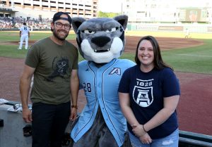 Young man and woman smiling and standing with AU mascot at baseball game
