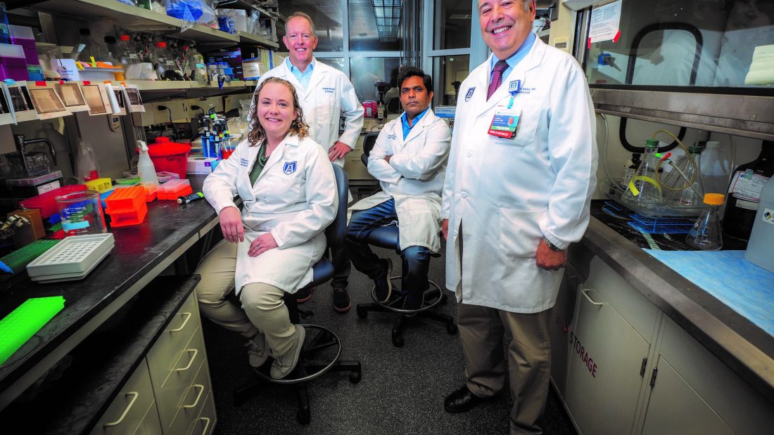 Four people in white coats stand in lab