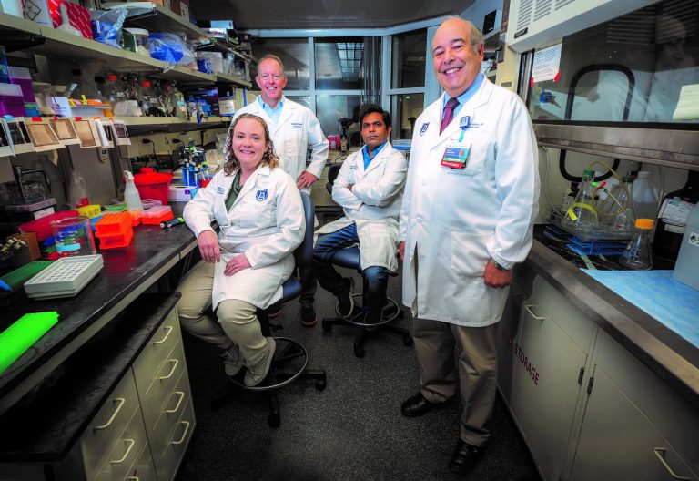 Four people in white coats stand in lab