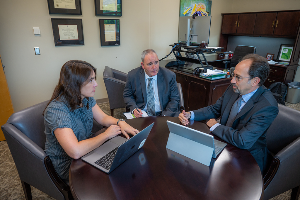 Two men and one woman sit in an office and hold a meeting. 