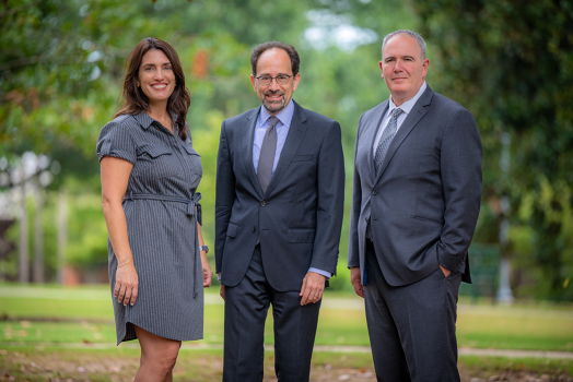 two men and a woman stand and smile for a photo oustide
