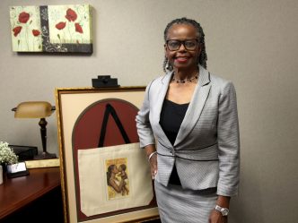Woman in gray suit stands next to framed photo