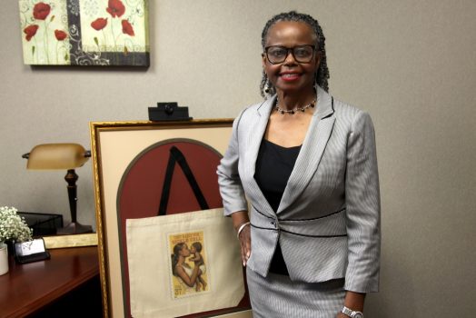 Woman in gray suit stands next to framed photo
