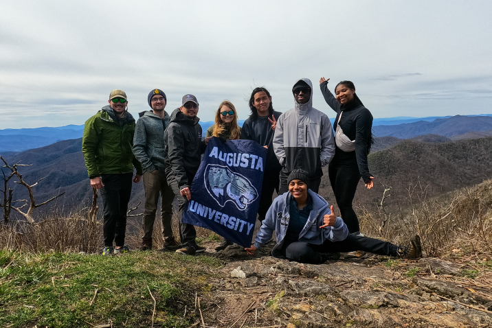 group of people standing on top of big hill with a mountain in the background