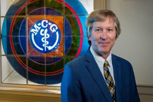 Man in blue suit stands in front of circular stained glass window