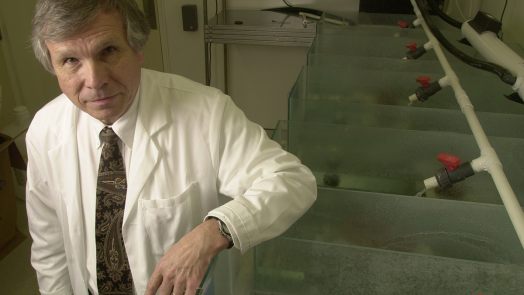 man in lab coat stands with one arm resting on a water tank