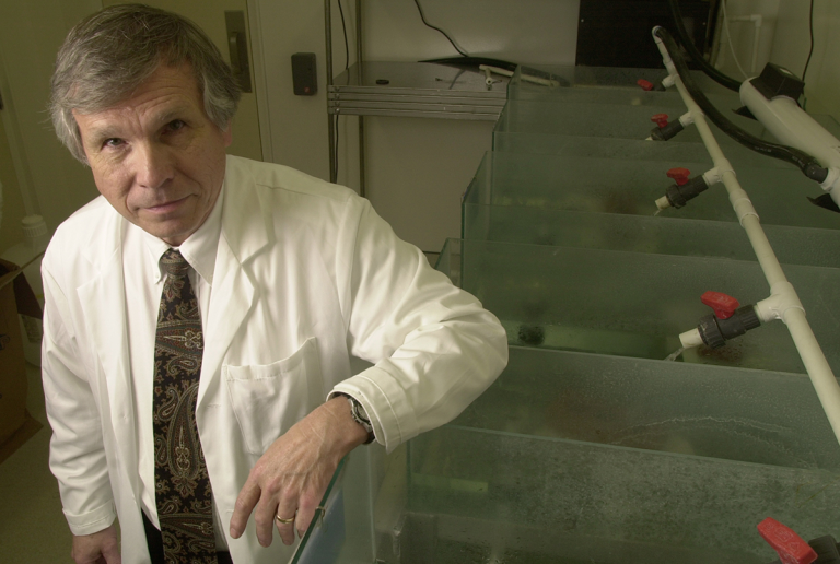 man in lab coat stands with one arm resting on a water tank