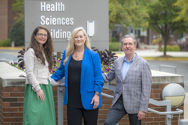 Three people in front of health sciences sign