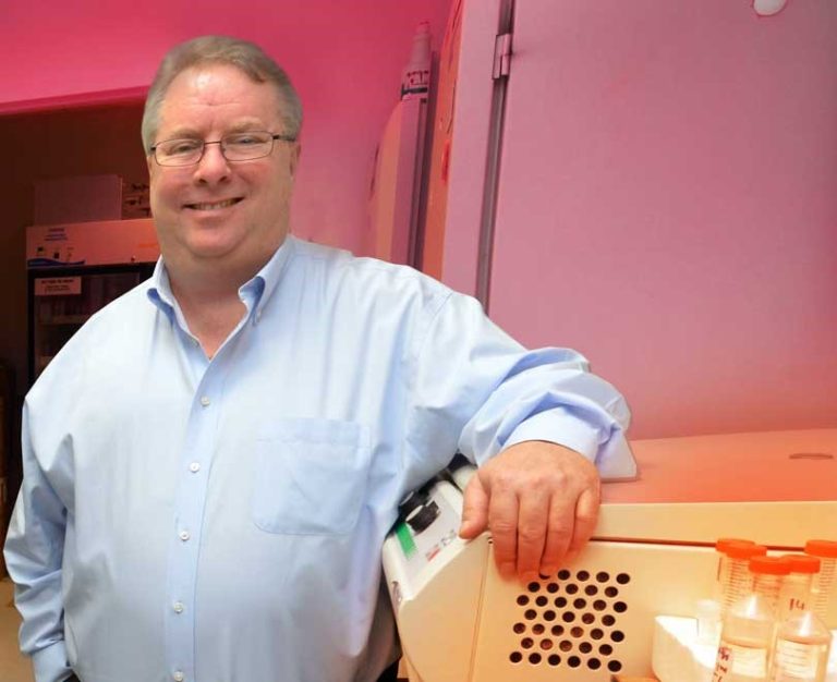 Man in blue shirt and glasses stands with elbow propped on computer