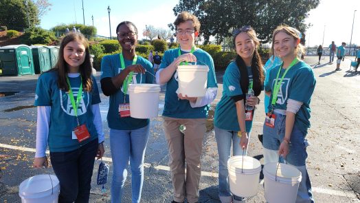 five students hold white buckets and smile at the camera