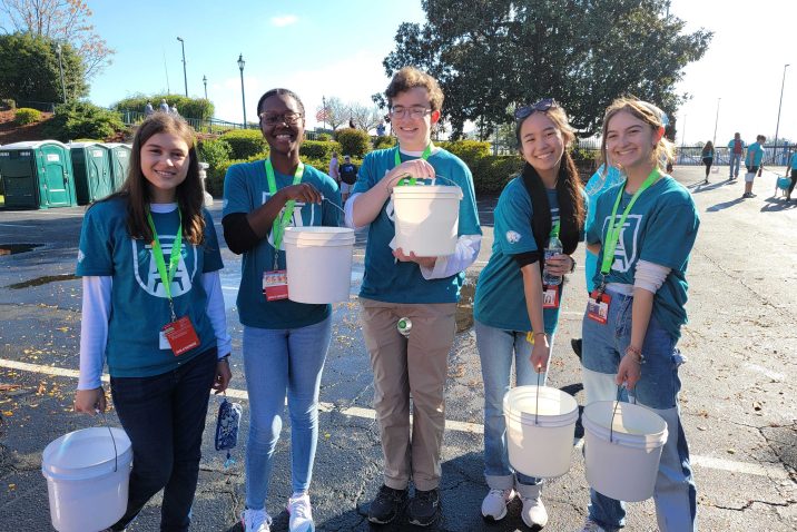 five students hold white buckets and smile at the camera