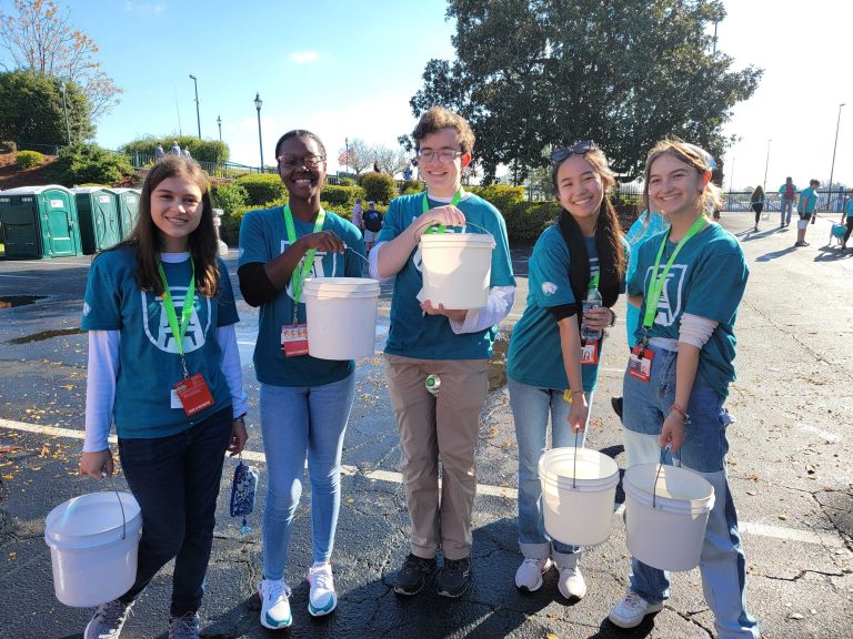 five students hold white buckets and smile at the camera