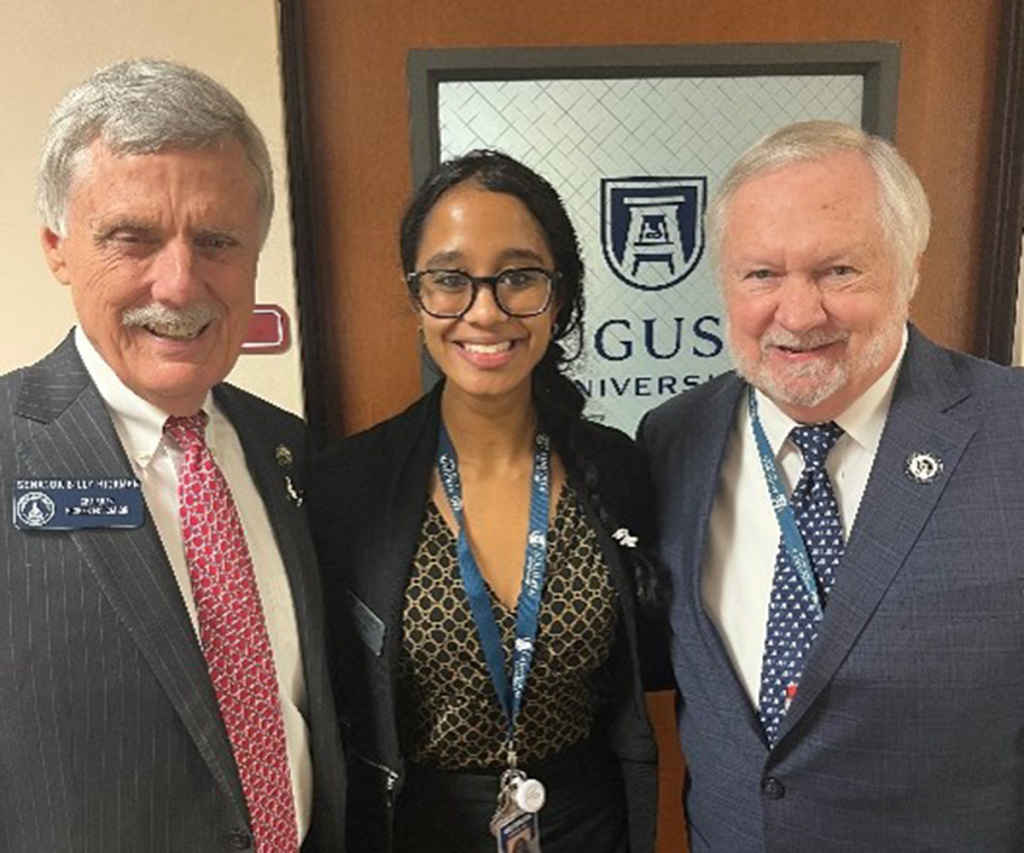 two men and one woman stand in front of a door smiling for a photo.