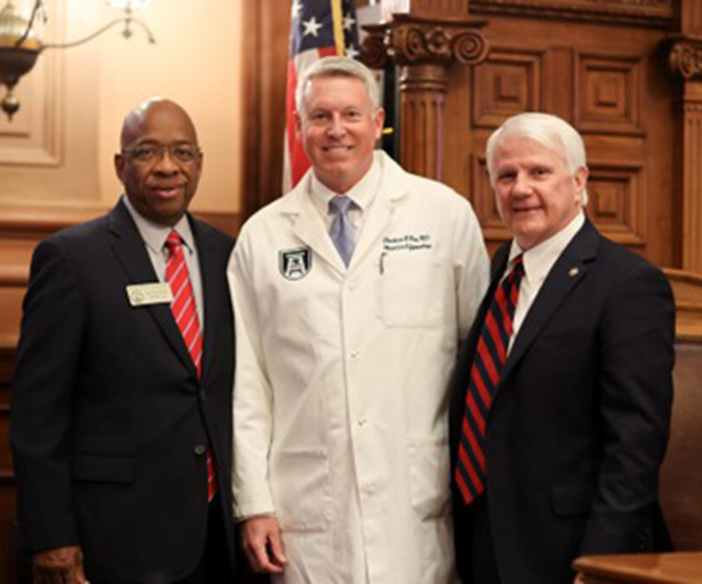 three men, one wearing a doctor's coat, pose for a photo in a large room.