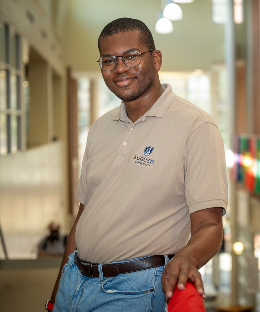 man with glasses wearing a polo leans against a railing for a photo