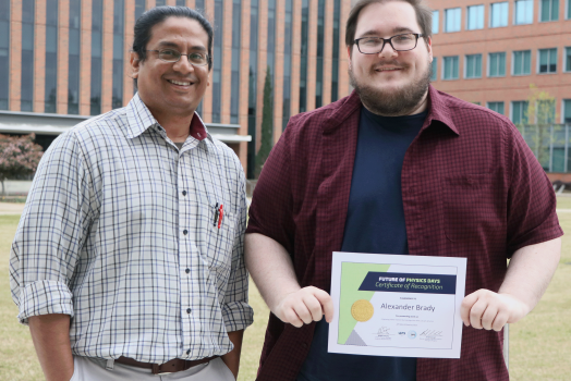 A professor standing next to his student while the student holds an award