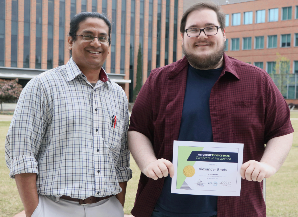 A professor standing next to his student while the student holds an award