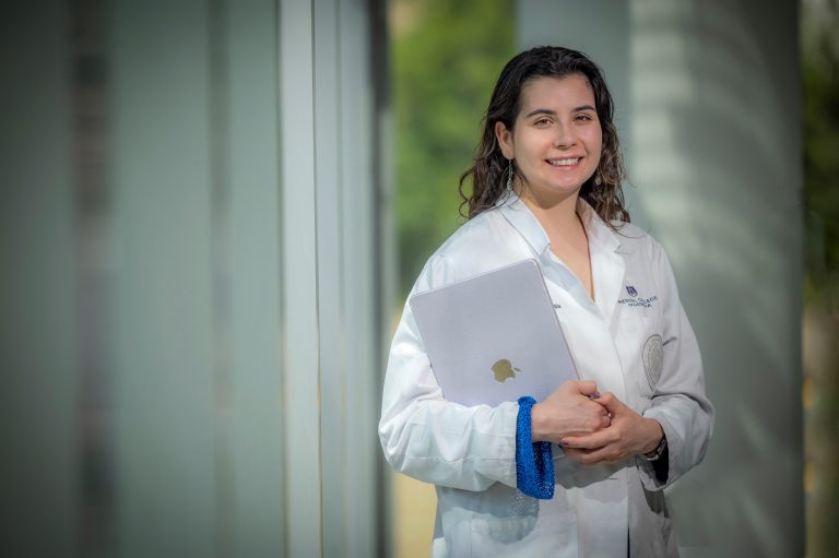 Woman in white coat holding computer stands in window