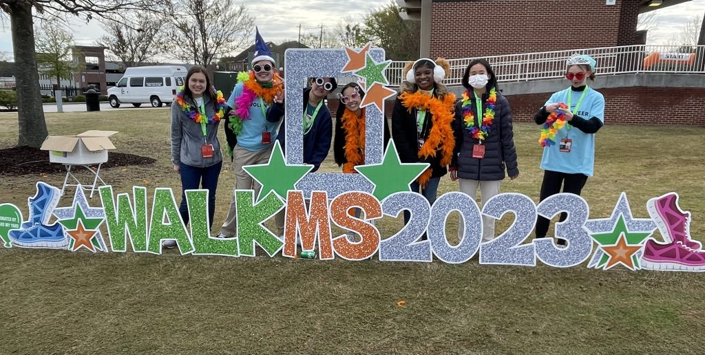 A group of students with leis stand in front of a sign that says Walk MS 2023