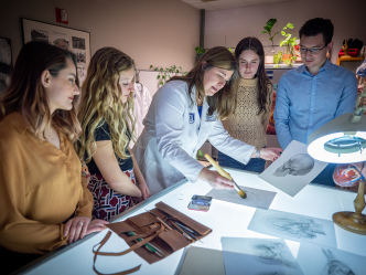 four women and one man gather around a table looking at drawings of human anatomy