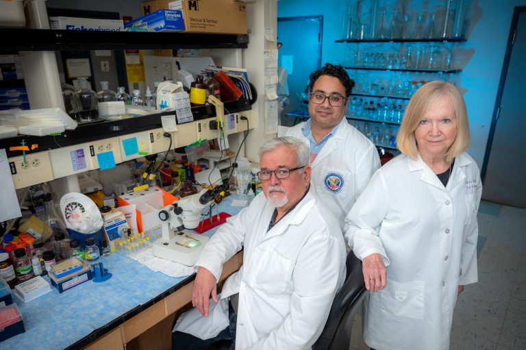 Three people in white coats stand in lab
