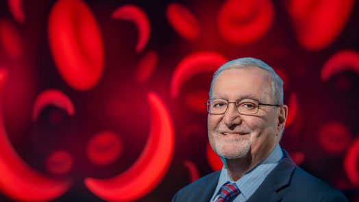 Man in suit and glasses poses in front of red blood cells