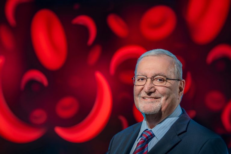 Man in suit and glasses poses in front of red blood cells