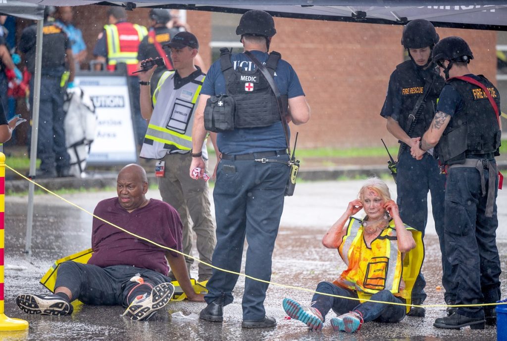 Actors serving as victims sit on the ground outside a school 