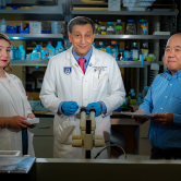 two men and a woman standing in a science lab smiling for the camera
