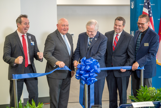 four men watch as a fifth cuts a ceremonial ribbon with large scissors