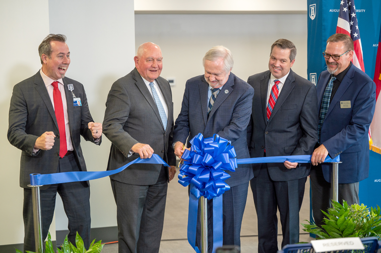 four men watch as a fifth cuts a ceremonial ribbon with large scissors