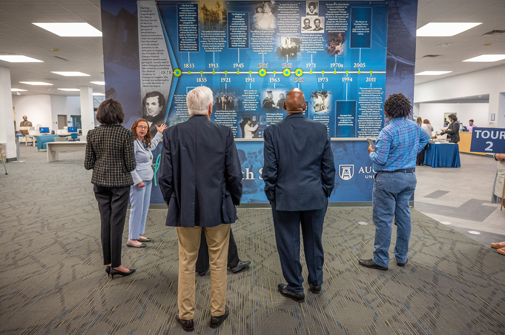 A group of people look at a series of graphics depicting the timeline of the Medical College of Georgia and the Robert B. Greenblatt, M.D. Library.