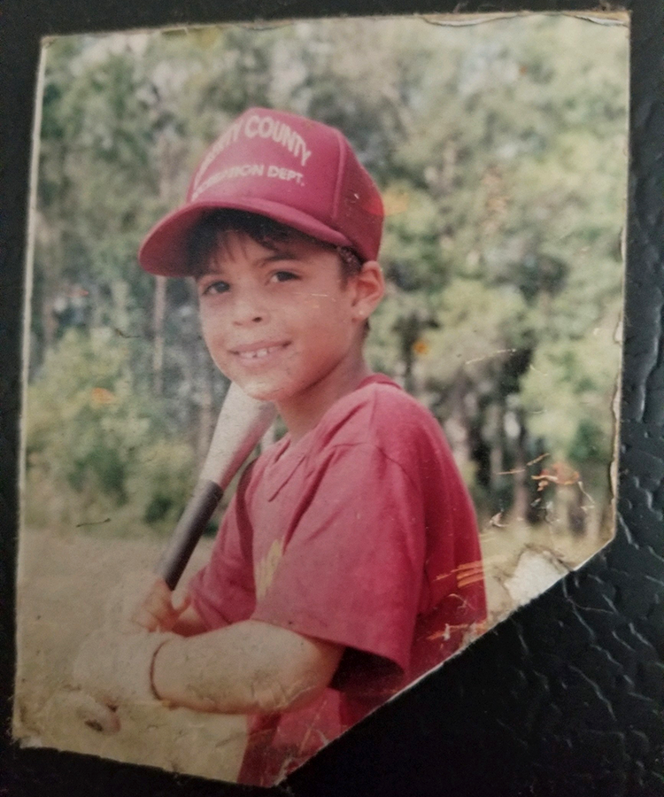 young boy  wearing a baseball uniform poses with a bat for a photo