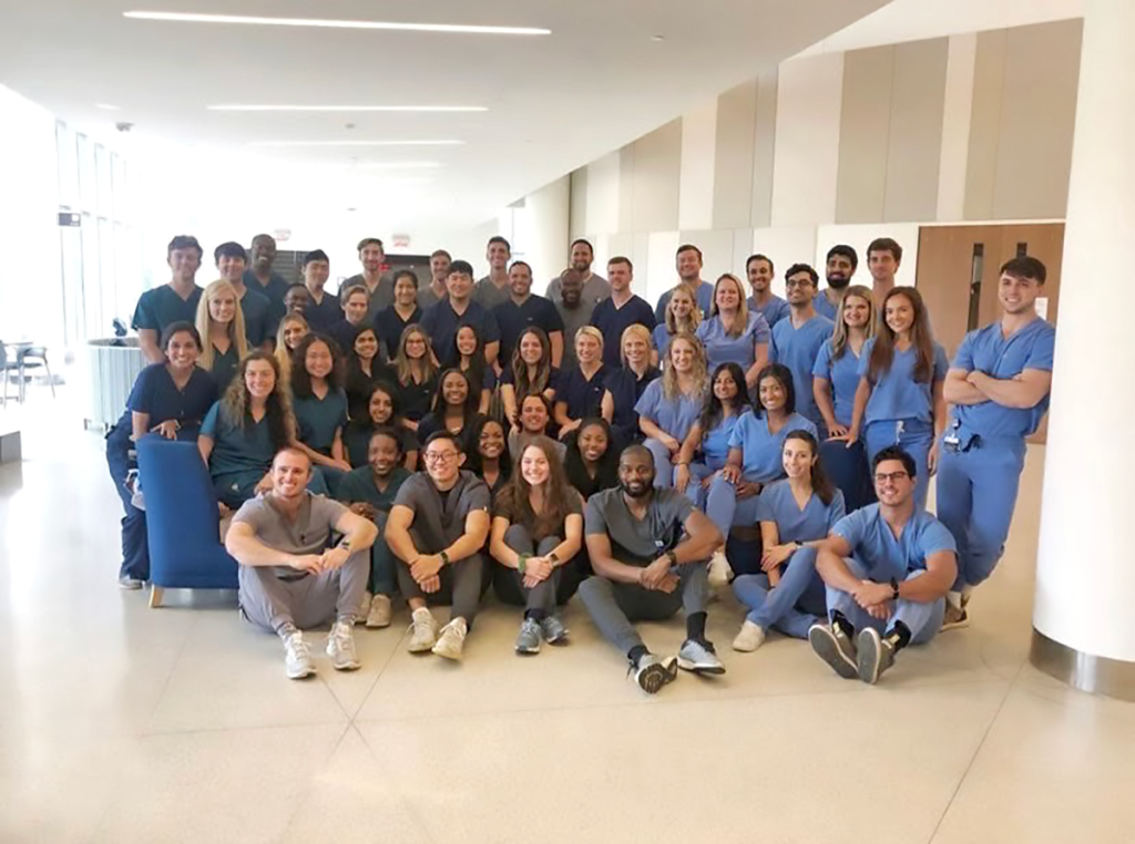 large group of students in scrubs pose for a photo in a large hallway