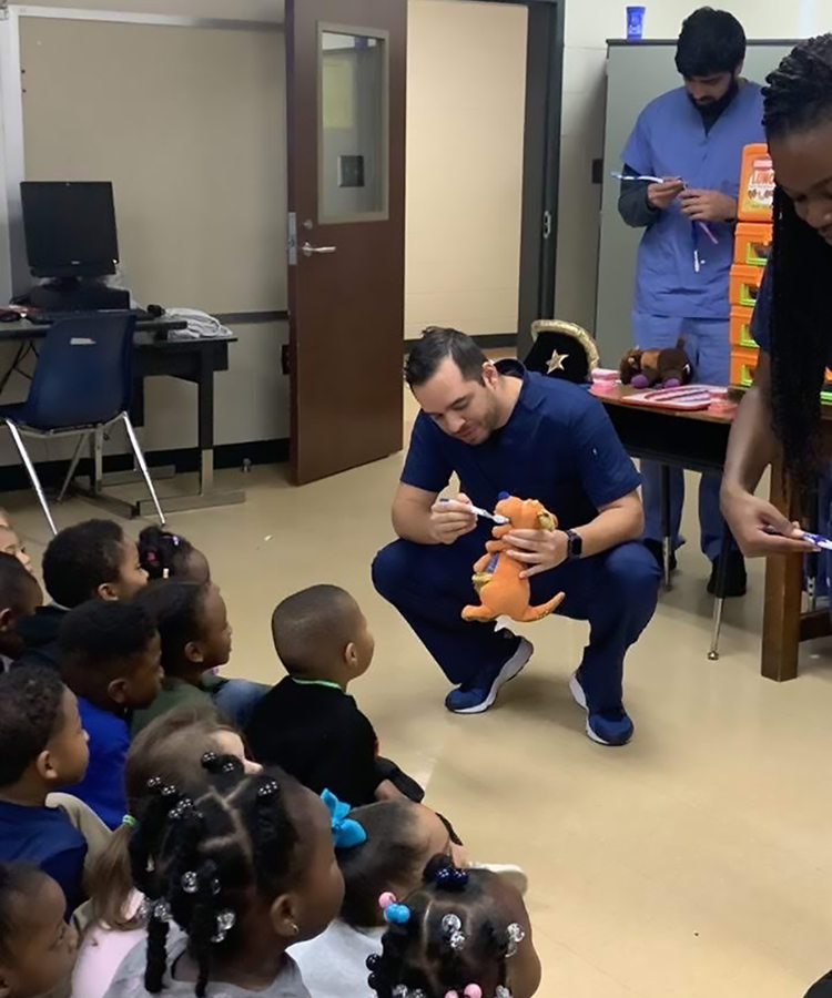 a male dentist uses a tooth brush on a stuffed animal while young children look on