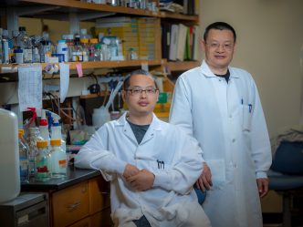 Two men in white coats sit in front of lab